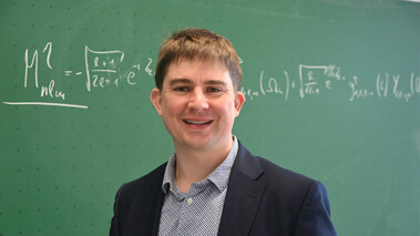 Simon Moser steht vor einer Tafel mit physikalischen Gleichungen, ausgezeichnet für gute Lehre.